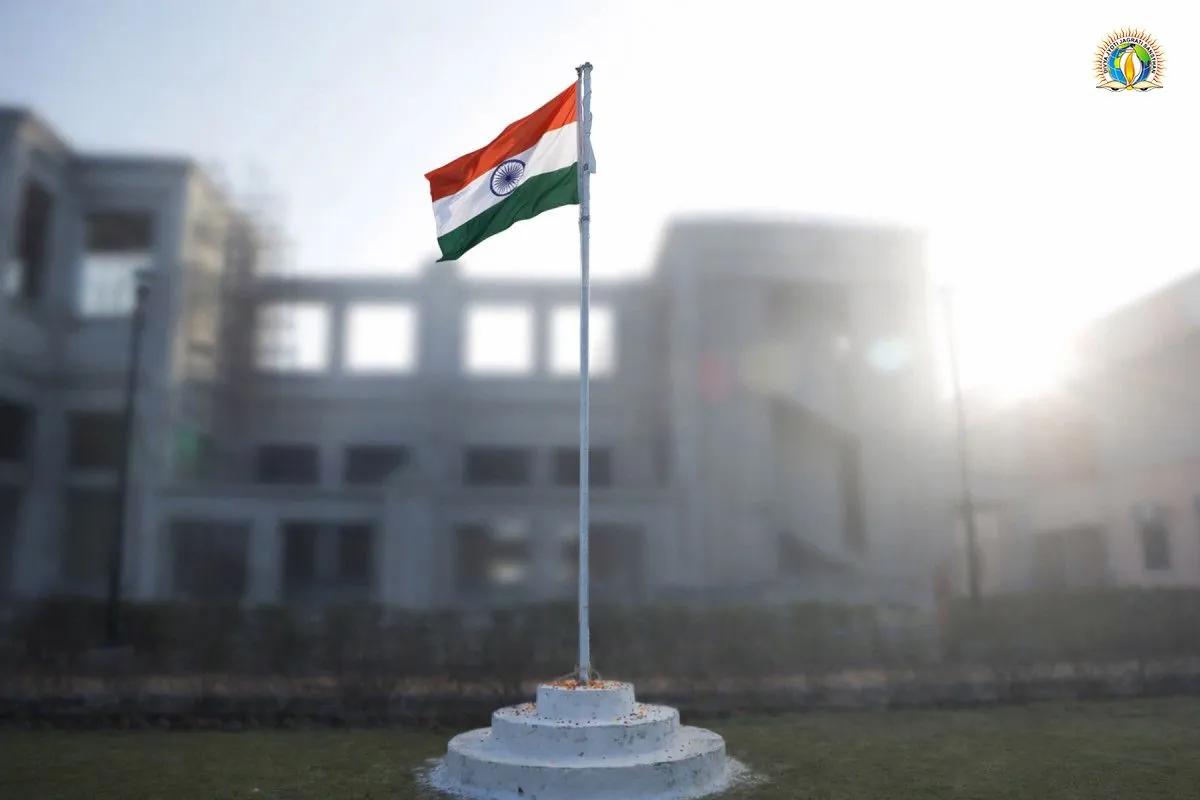The national flag flying over a white pedestal on the lawn of Divya Dham Ashram, the ashram building soft in the morning haze